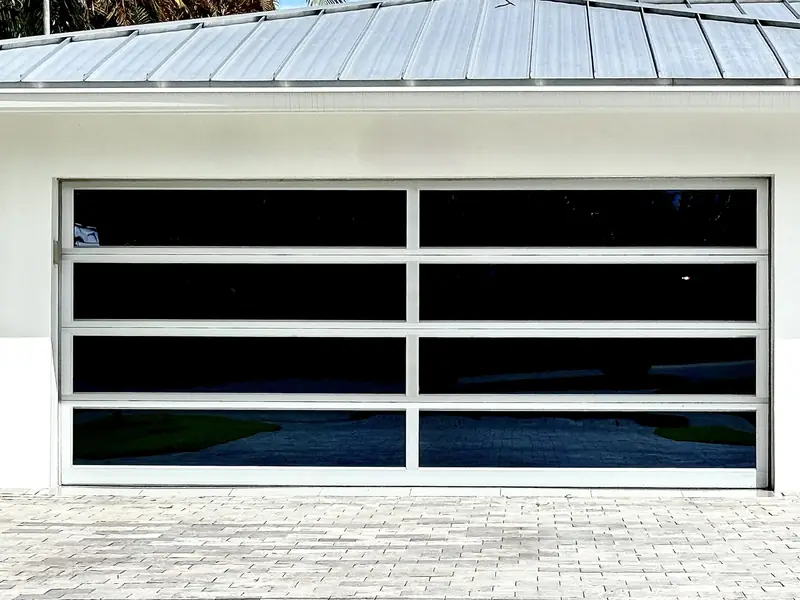 Wide two-car glass garage door with a white frame and dark glass under a metal roof